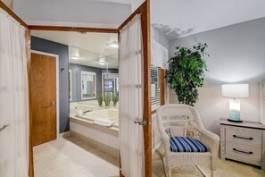 Un bagno con una vasca, una sedia in vimini, un comodino con una lampada e un'ampia pianta in vaso.