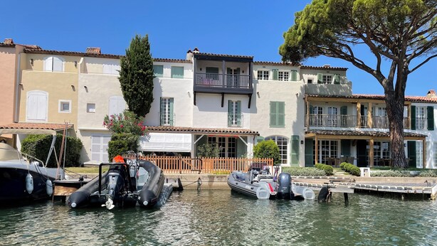 Un canal con barcos amarrados, edificios con balcones y un árbol grande.