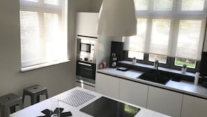 Une cuisine moderne équipée d’un four encastré, d’un évier et d’une grande fenêtre avec des stores.