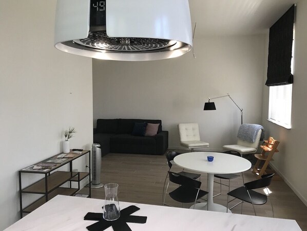 A modern, compact living space with a central table, chairs, a sofa, and a standing heater.