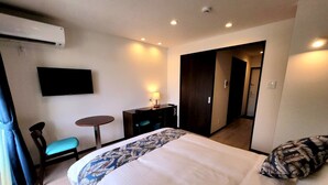 A hotel room with a bed, a desk, a chair, a TV, and an air conditioning unit. - PRIME TREE Izumizaki CONDO HOTEL (Naha)