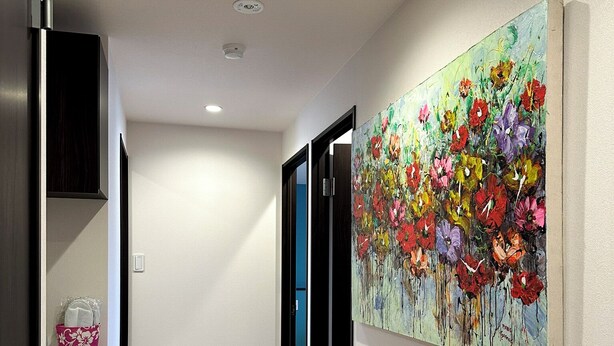 A hallway with a wooden floor, a painting of flowers on the wall, and a door leading to another room. - PRIME TREE Izumizaki CONDO HOTEL (Naha)