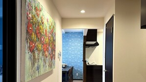 A hallway with a dining area, a kitchen, and a large abstract painting on the wall. - PRIME TREE Izumizaki CONDO HOTEL (Naha)