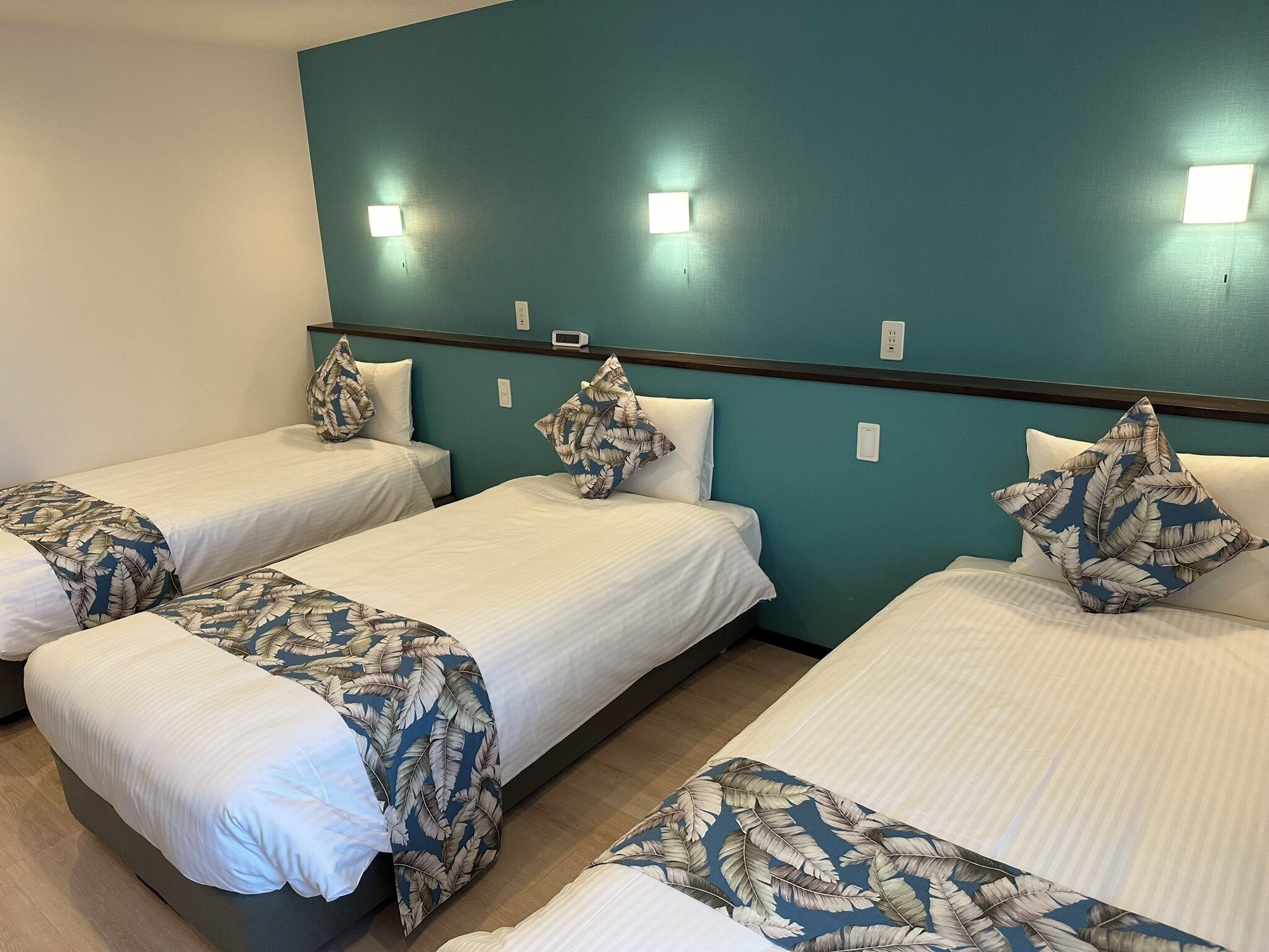 A hotel room with three single beds, each with a leaf-patterned bedspread and matching pillows.