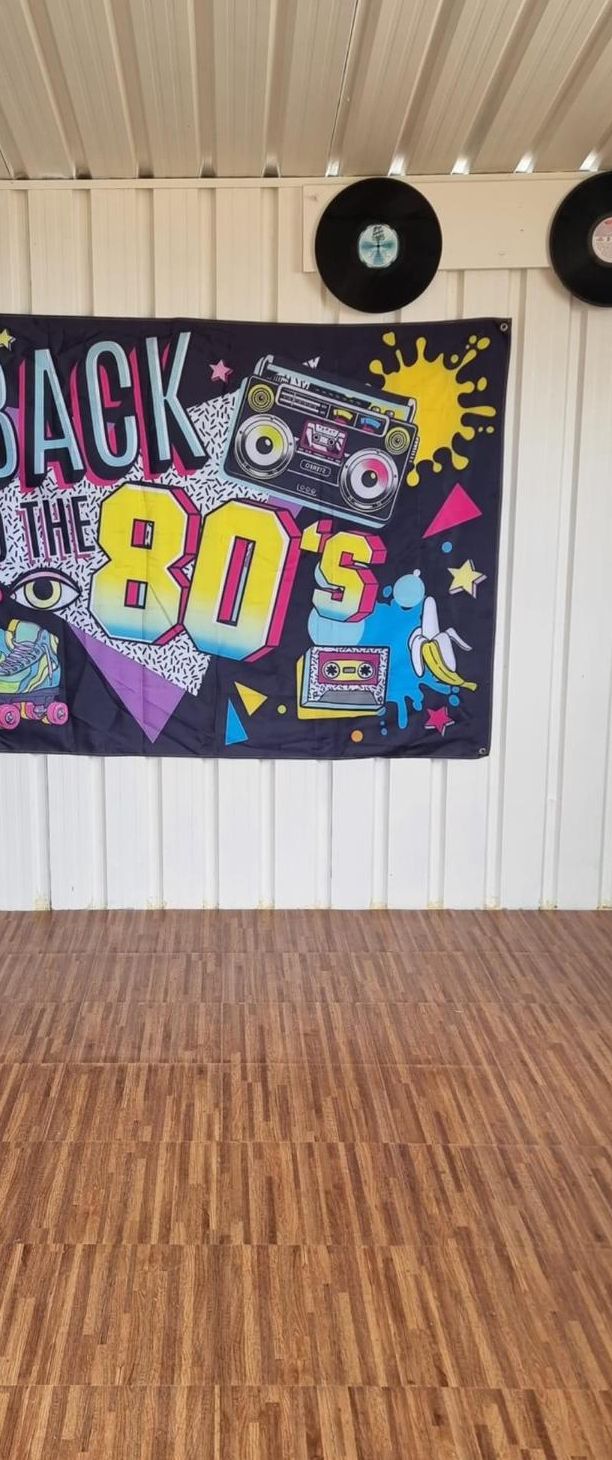A room with a wall decorated with a retro-themed banner, wooden flooring, and two vinyl records on the wall.