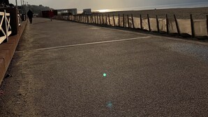 Un paseo marítimo con baranda de madera, faroles y cielo despejado con el sol poniéndose.