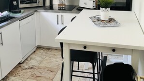 Una cocina moderna con armarios blancos, una campana de acero inoxidable, un microondas, un tostador y una pequeña planta en maceta sobre la encimera.