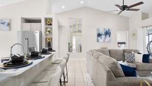 A modern kitchen with a central island, bar stools, and a grey sofa in the living area. - Beautiful 3BR Home Heated Pool | Ping-Pong |Disney (Davenport)