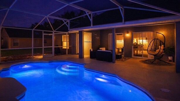 A swimming pool with a covered patio area, a hanging chair, and a well-lit interior space. - Beautiful 3BR Home Heated Pool | Ping-Pong |Disney (Davenport)