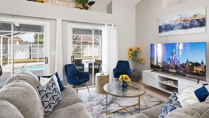 A spacious living room with a large TV, comfortable seating, and a view of the backyard. - Beautiful 3BR Home Heated Pool | Ping-Pong |Disney (Davenport)