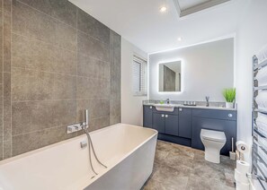 Ein modernes Badezimmer mit einer freistehenden Badewanne, einer Toilette und einem Waschtisch mit Spiegel.