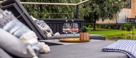 A modern outdoor seating area with a black sofa, a wooden table with two glasses, and a small potted plant.