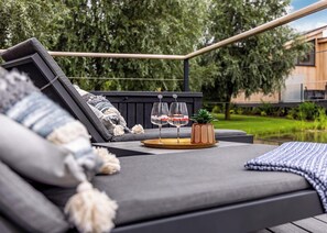 A modern outdoor seating area with a black sofa, a wooden table with two glasses, and a small potted plant. - Water Lily Lakeside Lodge (Boston)