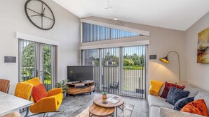 A modern living room with a TV, sofa, chairs, and a dining area. - Water Lily Lakeside Lodge (Boston)