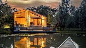 A wooden cabin with a deck, a small boat, and a reflection in the water. - Water Lily Lakeside Lodge (Boston)