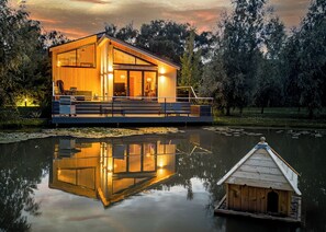 Eine Holzhütte mit einer Terrasse, einem kleinen Boot und einem Spiegelbild im Wasser.