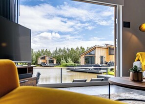 A modern interior with a large window overlooking a water body and two wooden buildings. - Water Lily Lakeside Lodge (Boston)