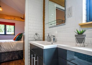 Ein modernes Badezimmer mit weiß gefliesten Wänden, einer Duschkabine aus Glas, einem Waschbecken mit Spiegel und einer Zimmerpflanze.