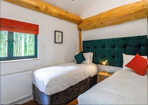 A bedroom with two beds, a window with a view of trees, a radiator, and a wooden ceiling.