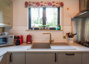 A kitchen with a window, a sink, a microwave, a kettle, and a gas stove.