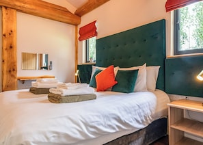 A bedroom with a large bed, wooden beams, a green upholstered headboard, and a window with a view of trees. - 2 bedroom accommodation in Ellesmere (Ellesmere)