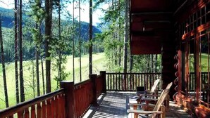 A wooden deck with a view of a forest and a distant hill. - EXCLUSIVE very private cabin on the golf course! (Panorama)