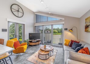 A modern living room with a TV, sofa, chairs, and a dining area. - Honeybee Lakeside Lodge (Boston)