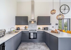 Une cuisine moderne avec des meubles de couleur sombre, un îlot central, un four encastré et des luminaires suspendus.