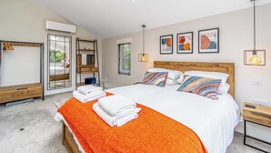 Un dormitorio con tragaluces, una cama con almohadones coloridos, una mesita de noche, un espejo y obras de arte en la pared.
