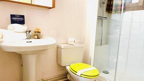 Ett badrum med ett vitt handfat, en toalett med ett gult sits och en duschkabin med glasväggar.