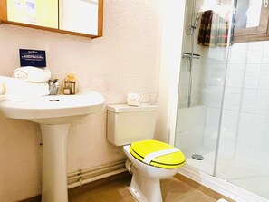 A bathroom with a white sink, a toilet with a yellow seat, and a glass shower enclosure.