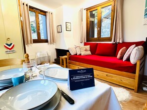 A cozy room with a red sofa, a dining table set with plates, glasses, and cutlery, and a sign in French.