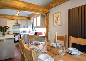 Un coin repas avec des chaises en bois et une table dressée pour le repas, une cuisine en arrière-plan et une tête de cerf encadrée accrochée au mur.