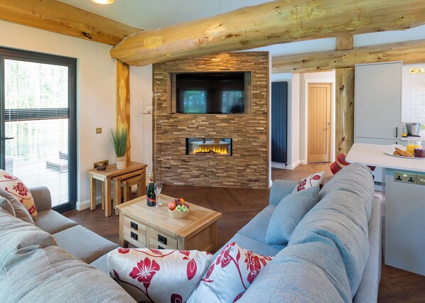 A modern living room with a stone fireplace, a television, and a dining area with a kitchen in the background.