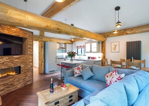 Un salon moderne avec une cheminée, un canapé, une table basse avec une bouteille et des verres, et une cuisine en arrière-plan.