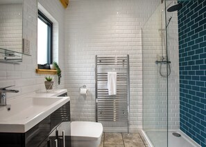 Une salle de bain moderne avec des murs recouverts de carreaux de céramique blancs rectangulaires, une douche en verre, un lavabo blanc et une porte de douche en verre.