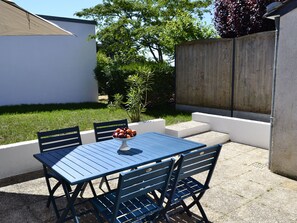 A patio with a table and chairs, a bowl of fruit, and a wooden fence in the background. - Charming 2-Bedroom Cottage Near Guérande and La Baule Beaches, with Terrace and WiFi (Guérande)