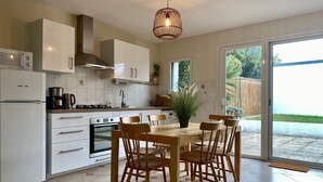 A modern kitchen with white cabinetry, a built-in oven, a coffee maker, and a dining table with chairs. - Charming 2-Bedroom Cottage Near Guérande and La Baule Beaches, with Terrace and WiFi (Guérande)