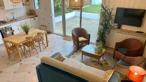 A modern living room with a sofa, a dining table with chairs, a TV, and a kitchen area with a sink and stove. - Charming 2-Bedroom Cottage Near Guérande and La Baule Beaches, with Terrace and WiFi (Guérande)