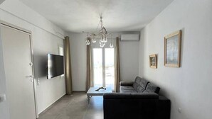 A modern living room with a flat-screen TV, a sofa, a coffee table, and a chandelier.