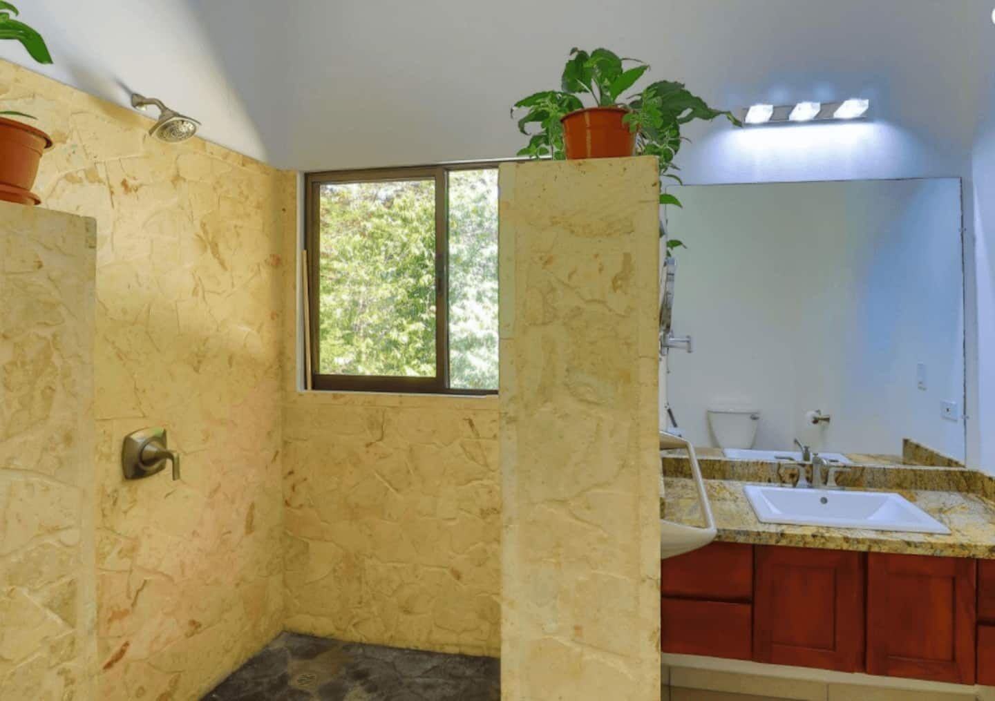 A bathroom with a shower, a window, a sink, and cabinets.