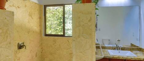 A bathroom with a shower, a window, a sink, and cabinets.