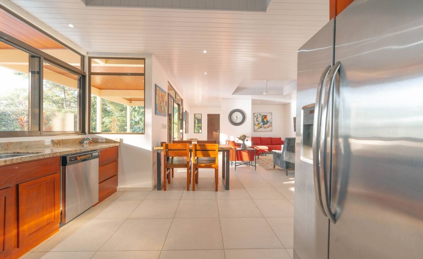 A modern kitchen with wooden cabinets, a stainless steel refrigerator, and a dining area with a table and chairs.