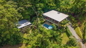 A two-story house with a swimming pool, surrounded by dense greenery.