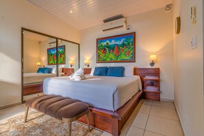 A hotel room with a large bed, a bench, a nightstand, a mirror, and a painting.