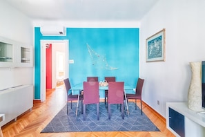 A modern dining area with a blue accent wall, a dining table with chairs, and a kitchen area with white cabinets.