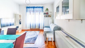 A modern living room with a sofa, a TV, a bookshelf, and a window with curtains. - GuestHost - JJ'S Place Trieste Apartment (Trieste)