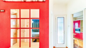 A hallway with a red wall, a door with a frosted glass panel, and a glimpse of a kitchen area with red cabinets. - GuestHost - JJ'S Place Trieste Apartment (Trieste)