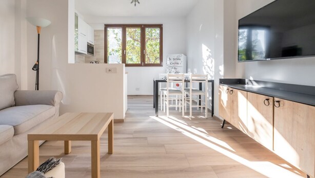 Eine moderne Küche mit Flachbildfernseher, ein Essbereich mit Tisch und Stühlen sowie eine Couch in einem hellen Wohnraum.