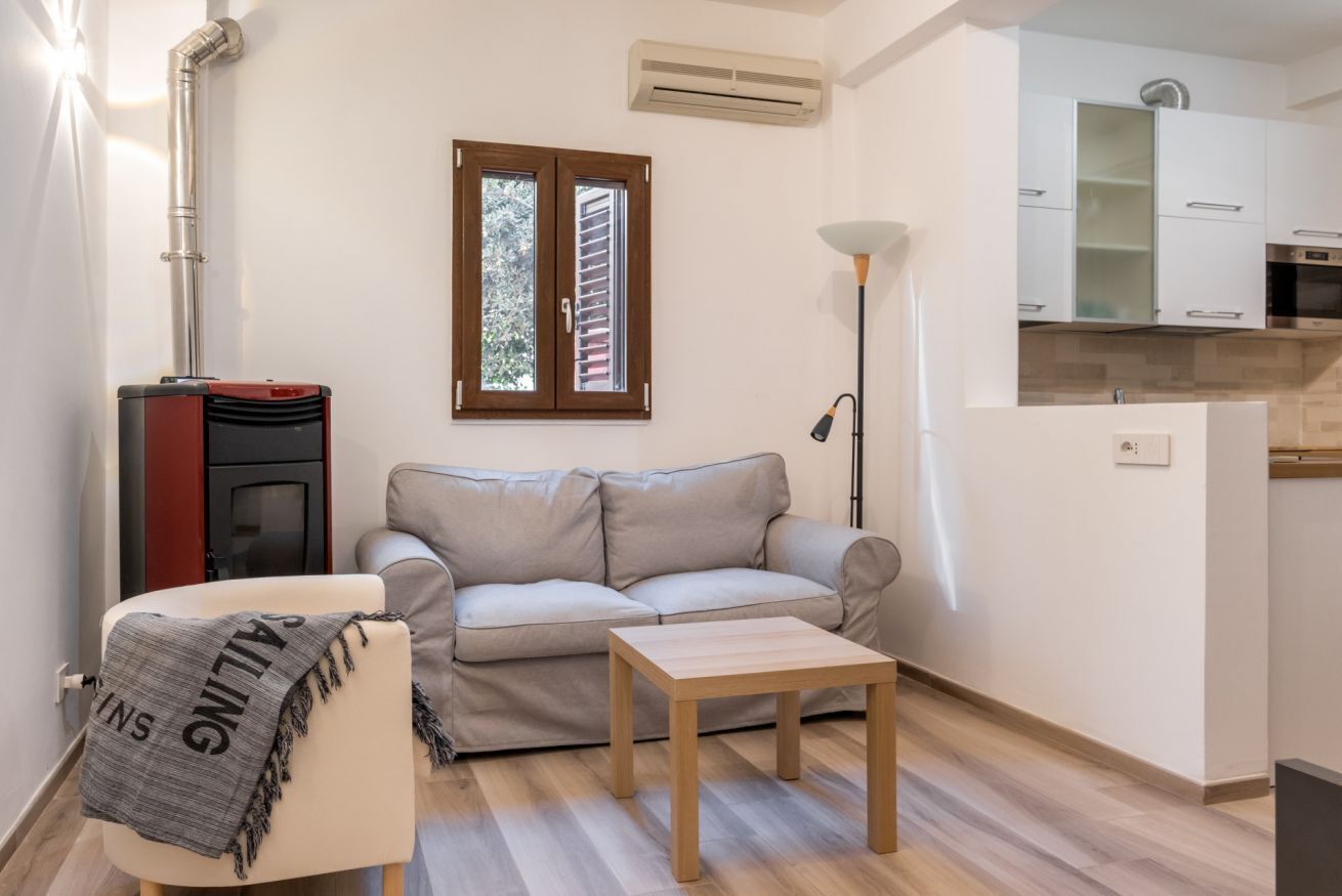 Un salon comprenant un canapé, une petite table, une lampe, une cheminée et un coin cuisine avec des placards.